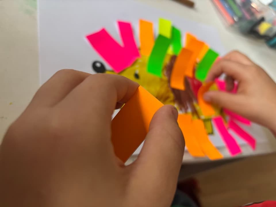 Detské ruky lepia farebné papieriky na obrázok leva.