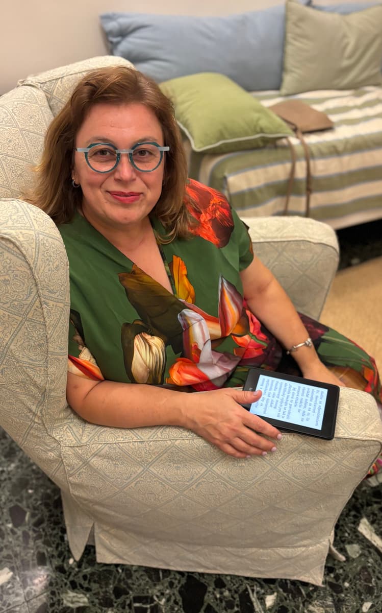 PaedDr. Monika Stupková, PhD., sedí v kresle s čítačkou kníh v ruke.